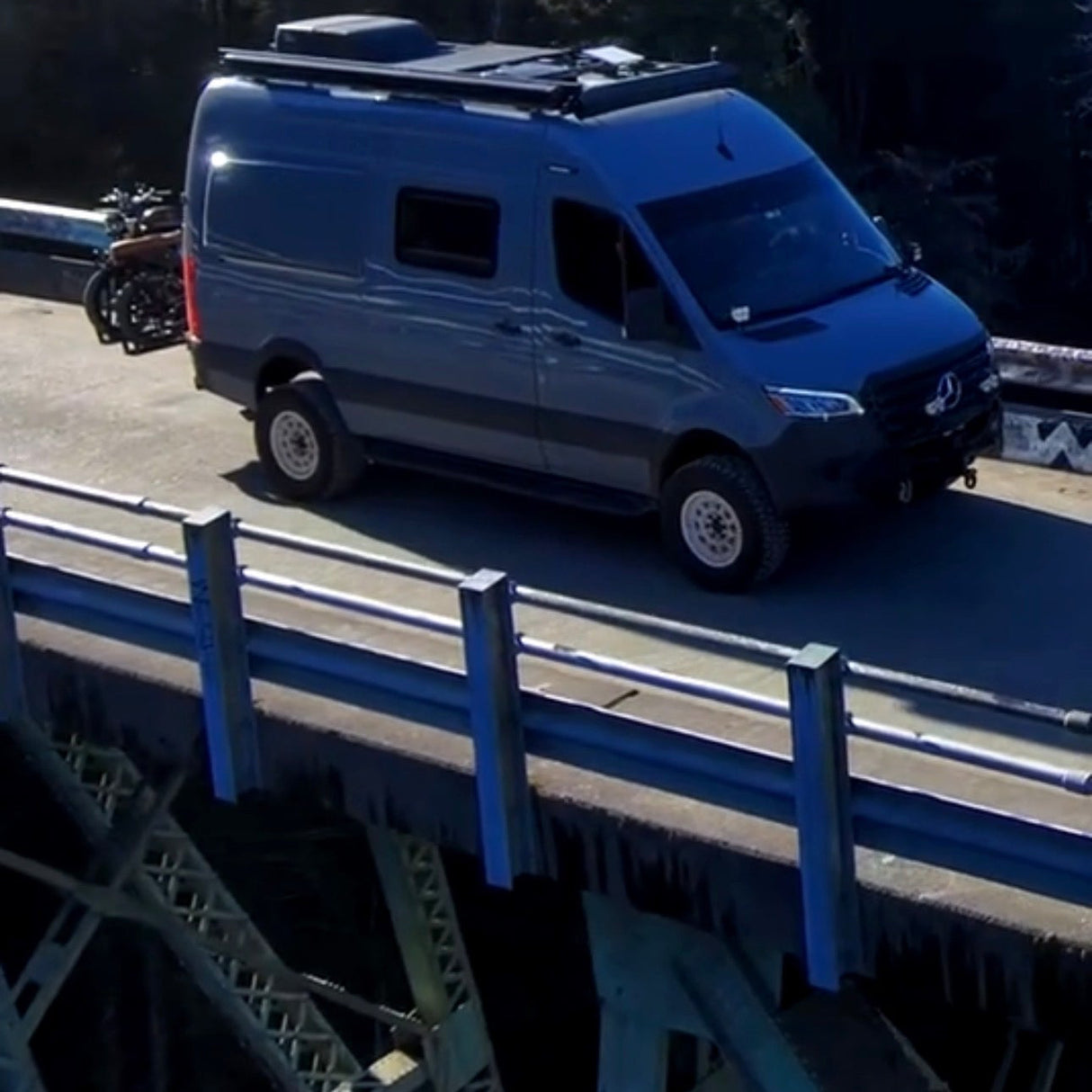 Blue van on a bridge with a forest in the background