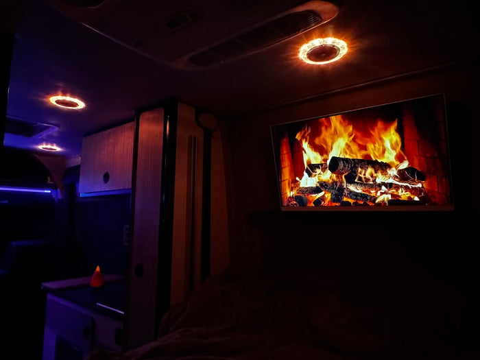Bedroom television showing a fireplace in a Winnebago Revel with warm interior lighting