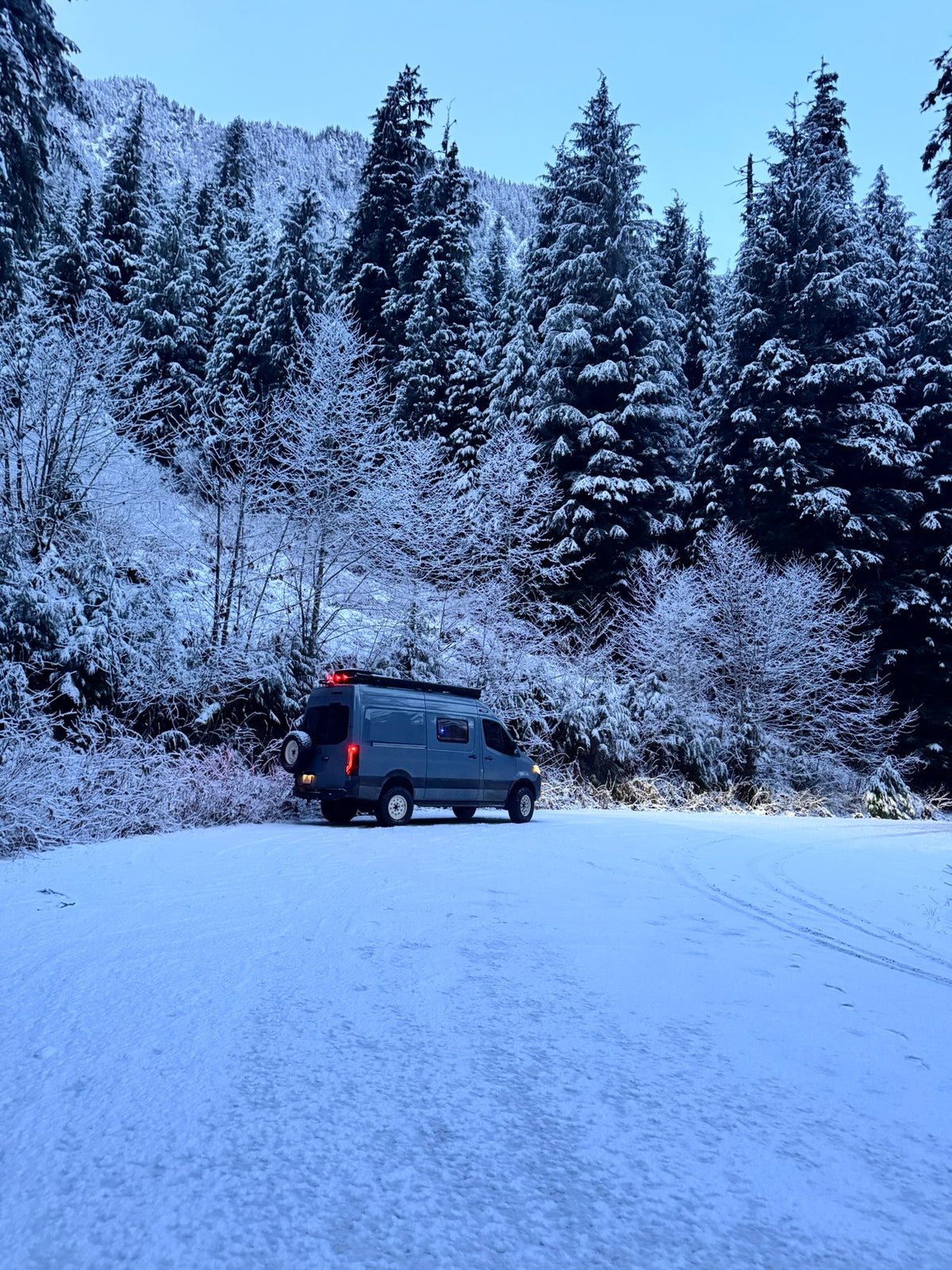 Adventure van parked in deep snow among snow-covered evergreen trees