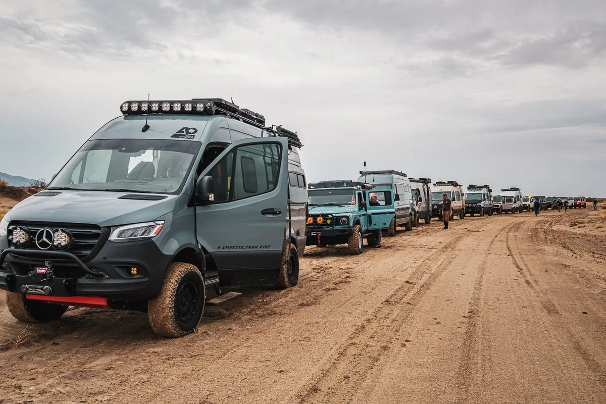 A convoy of Sprinter adventure vans and other overland vehicles gathered on a desert trail