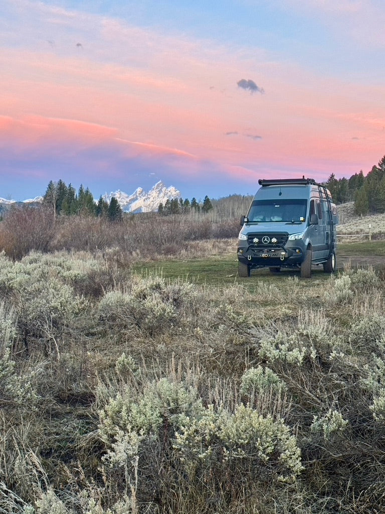 Wolf Pack's Winnebago Revel camping near the Tetons beneath a pink sunset sky.