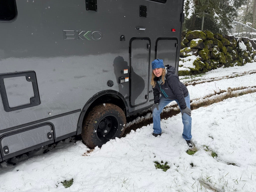 A woman giving a thumbs-up beside a Winnebago EKKO in the snow